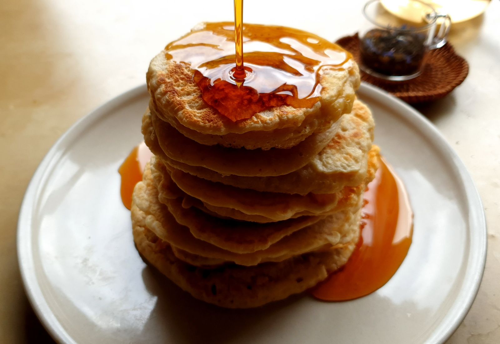 Tall stack of golden oat pancakes made with Oat-EH oat pancake and waffle mix, drenched in maple syrup